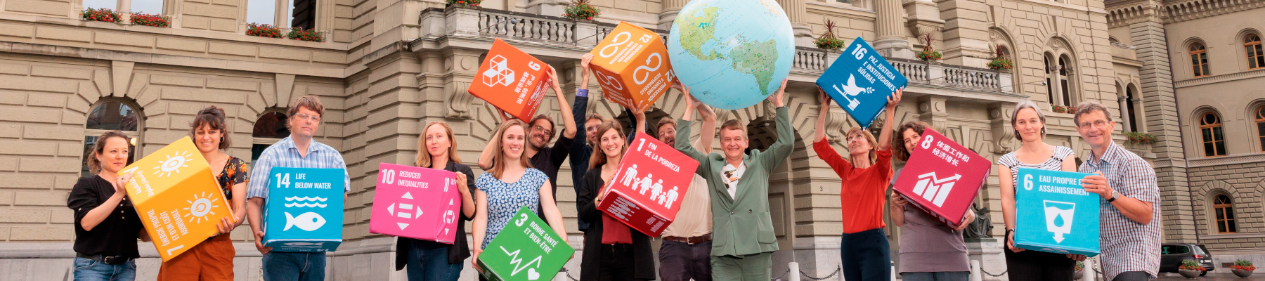 A group of people stands on the Bundesplatz with large SDG cubes and a large globe.